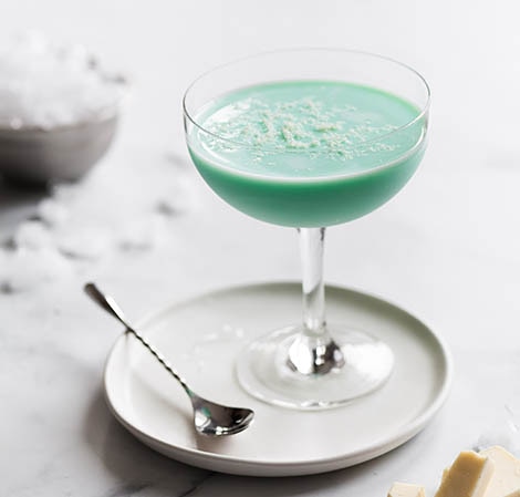 Bright green drink in a martini glass with white chocolate shavings on top