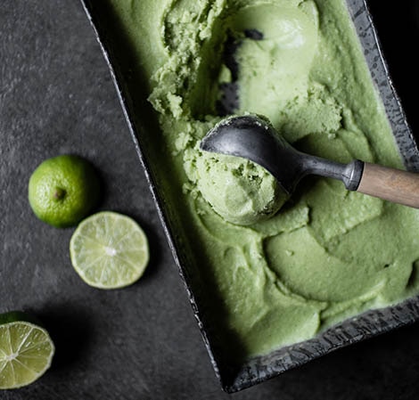 Crème glacée à la lime Key lime pie ice cream in a rectangular vessel being scooped out with some limes off to the side.