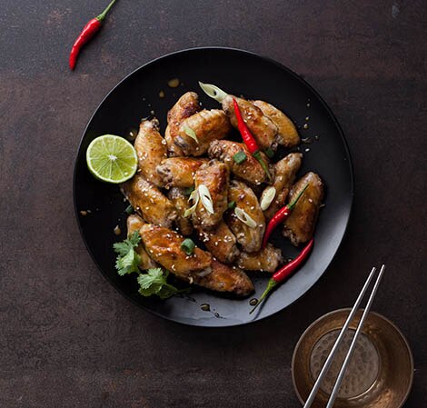 Asian inspired chicken wings in a bowl with chiles and a lime